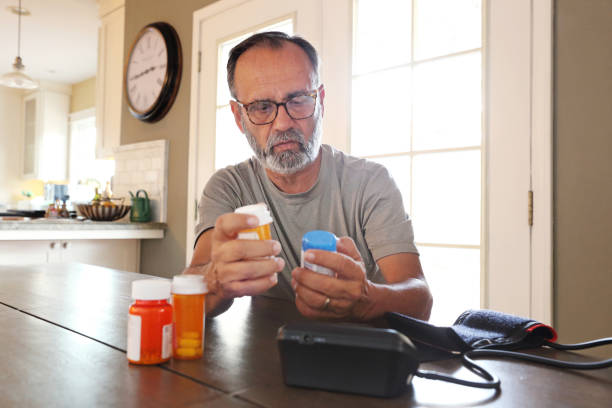 istock Latino Man Sitting At Table Sorting Through Prescription Medications 2163543764