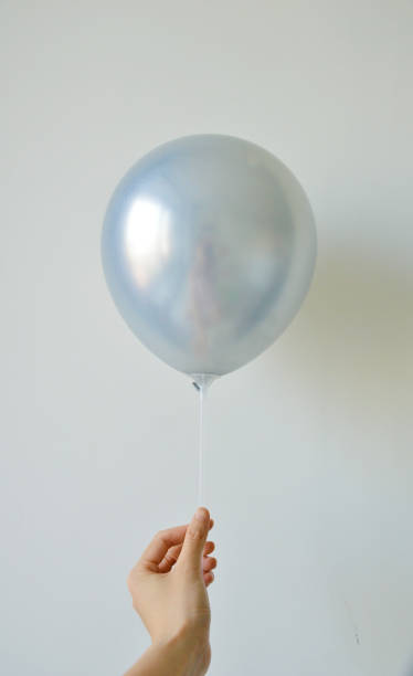 istock Cropped hand holding silver shiny balloons in white background 2163546176
