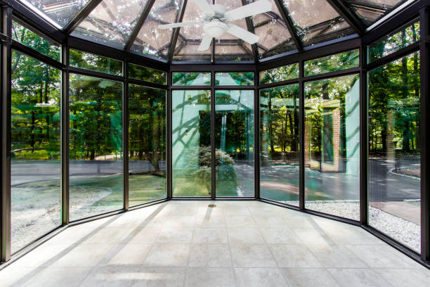 3D render captures the interior of a modern villa with large glass windows, offering a clear view of a swimming pool and lush trees outside. The design emphasizes openness and natural light.