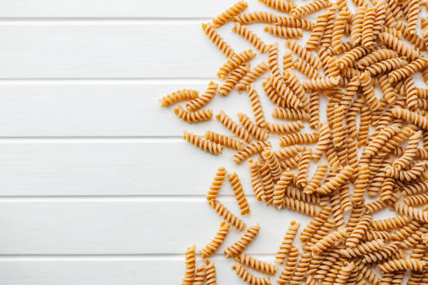 istock Uncooked whole grain pasta. Raw fusilli pasta on white table. Top view. 2163550205