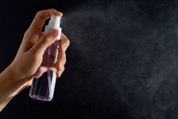 istock Hand holding cosmetic bottle spraying liquid, on black background 2163553075