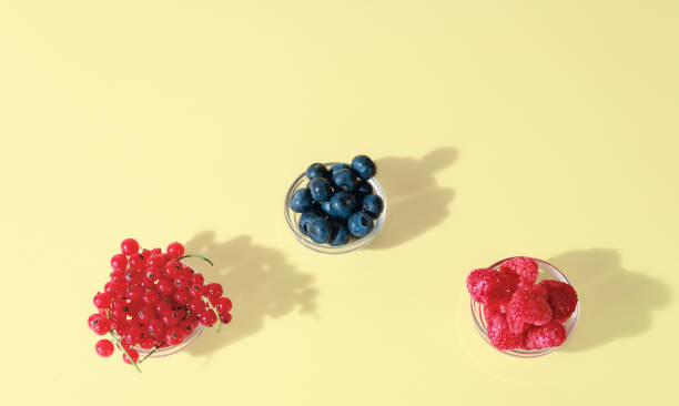 istock Three glass bowls with red Currants, Blueberries, and Raspberries on a light yellow background, minimal summer fruits concept 2163556609