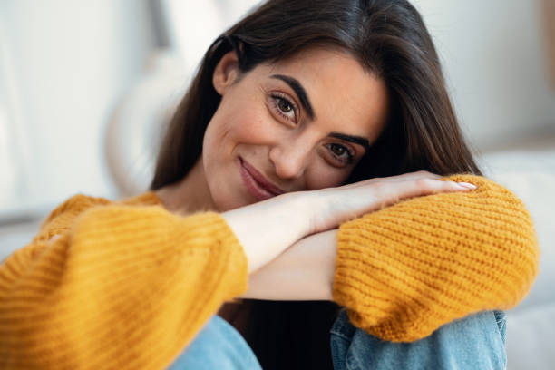 istock Cute young woman looking at camera while sitting on sofa at home. 2163567665