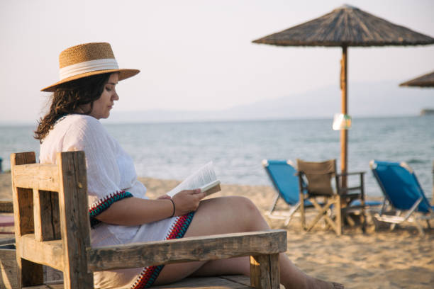 istock Young woman reading book on the beach 2163573390