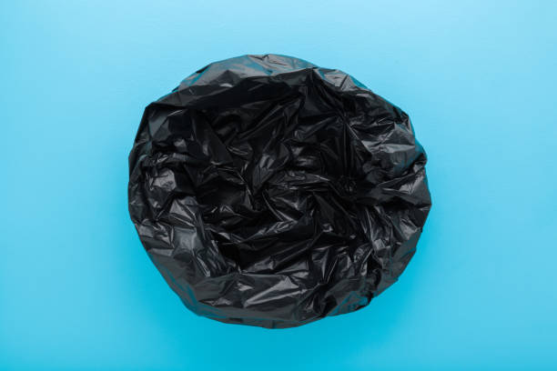 New empty dark black opened plastic garbage bag on light blue table background. Pastel color. Closeup. Top down view.