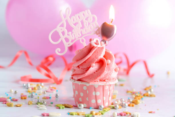 istock Pink birthday cupcake with a candle and balloons. Selective focus 2163578791