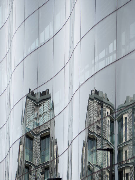 A modern boxy building seen reflected in the undulating wavy glass of a modern building