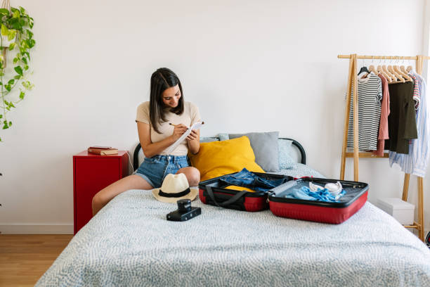 istock Young pretty woman doing checklist, preparing summer suitcase before vacation 2163587977