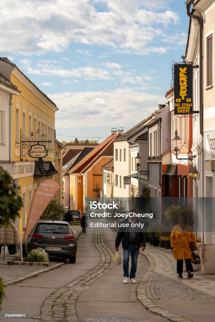 Cobblestone street in Melk, Austria, lined with colorful buildings and shops. Two people walk along the street. - Royaltyfri Dürnstein Bildbanksbilder Cobblestone street in Melk, Austria, lined with colorful buildings and shops. Two people walk along the street. - Royaltyfri Dürnstein Bildbanksbilder