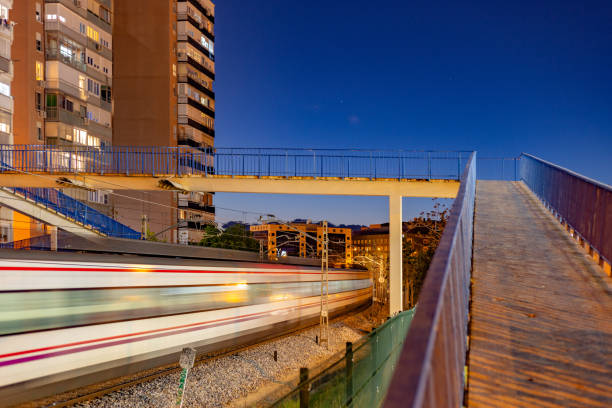 Madrid, Spain. Twilight scene of an elevated bridge over railway tracks with a train passing through in a suburban district.