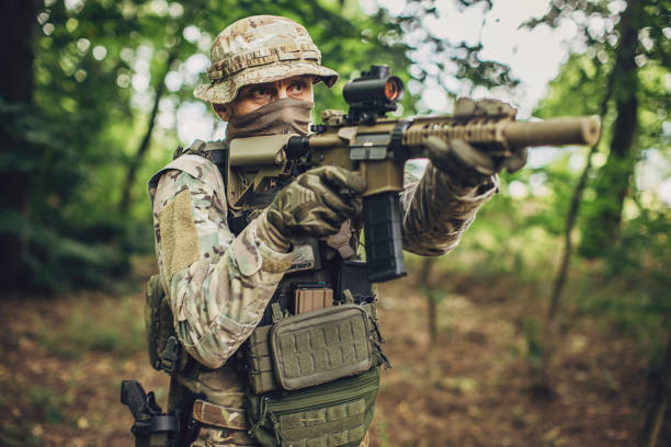 istock Soldier with rifle aiming through forest foliage. 2163601371