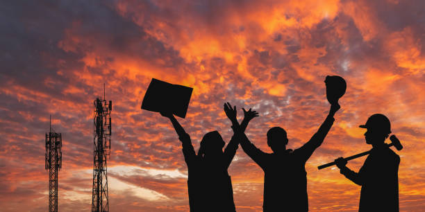 Success silhouette of Engineer and worker telecommunication tower holding blueprints controlling installation connectivity equipment maintenance sunset sky background.