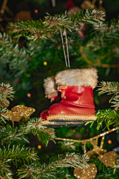 Santa Claus red boots ornament with a white fur trim hangs from a green Christmas tree.