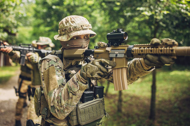 istock Masked soldier aiming rifle in forested area. 2163611315
