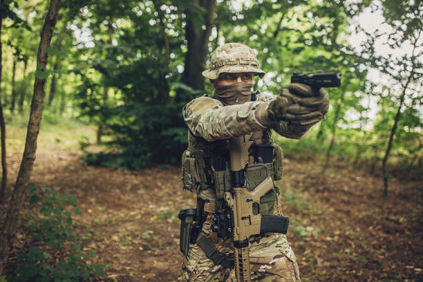 istock Soldier with drawn pistol and rifle strapped in forest. 2163612676