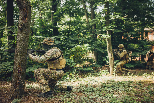 istock Soldier aiming rifle behind a tree in the forest 2163614770