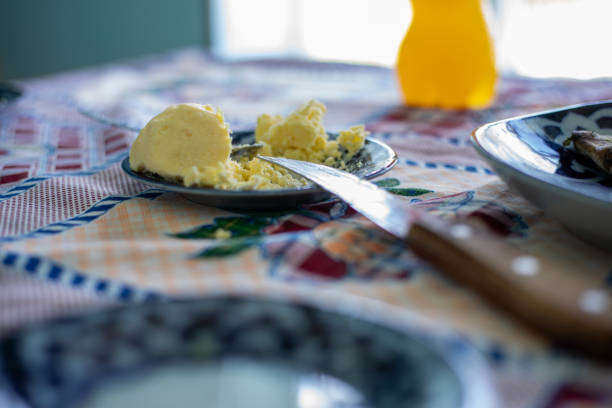 A plate of butter is on a table with a knife next to it. The butter is spread on a piece of bread