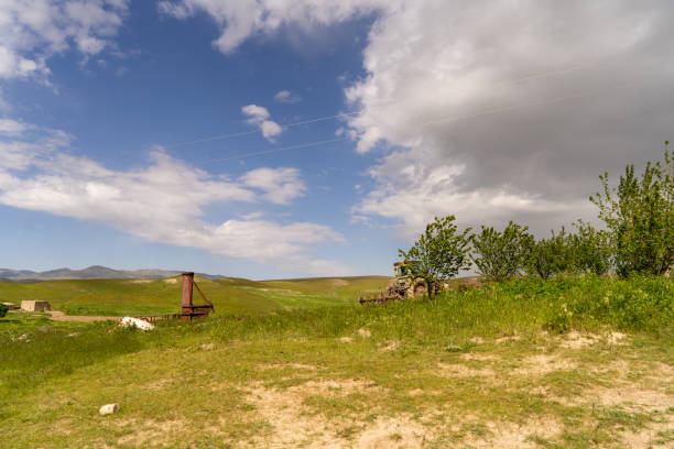 A field with a rusty old water pump and a few trees. The sky is mostly blue with some clouds