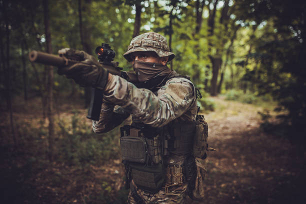 istock Soldier aiming rifle, tactical gear in forest setting. 2163625859