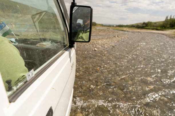 Adventurous traveler stands by SUV on rocky terrain. Scenic sunrise landscape with rugged 4x4. Solitary journey in remote desert region evokes wanderlust.