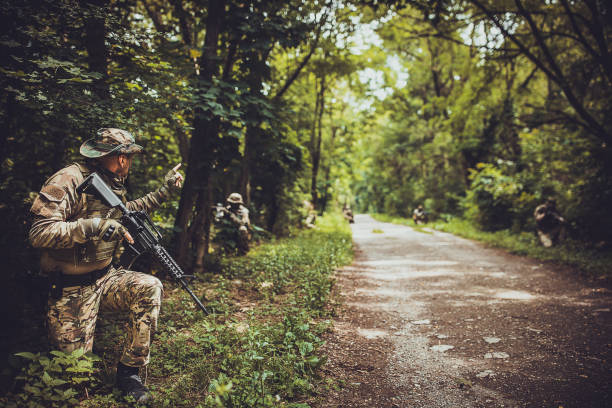 Soldiers holding rifles and adopting tactical positions along a forest road, showing military preparedness and strategic teamwork in a dense, green environment.