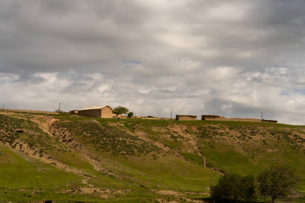 A cloudy sky with a house in the distance. The house is surrounded by a field of grass