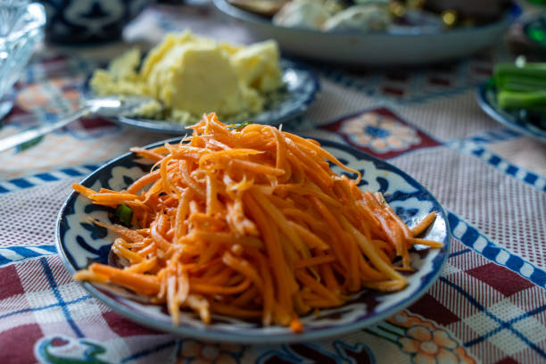 A plate of orange carrots is on a table. The carrots are sliced and arranged in a pile. The tablecloth is colorful and has a floral pattern