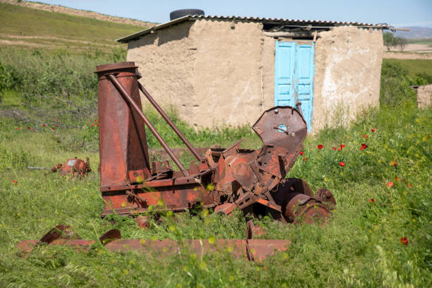 A rusty old tractor is sitting in a field next to a small house. The scene is quiet and peaceful, with the only sounds being the rustling of the grass and the occasional chirping of birds