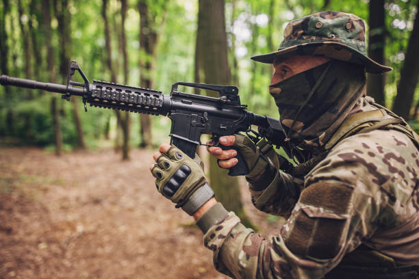 istock Camouflaged soldier aiming a rifle in forest environment 2163633115