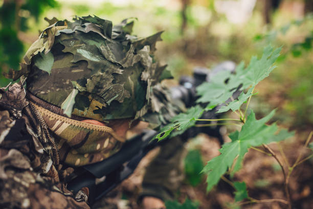 A Japanese hunter in Hokkaido wearing a Ghillie suit with his rifle in the snowy woodland portrait.