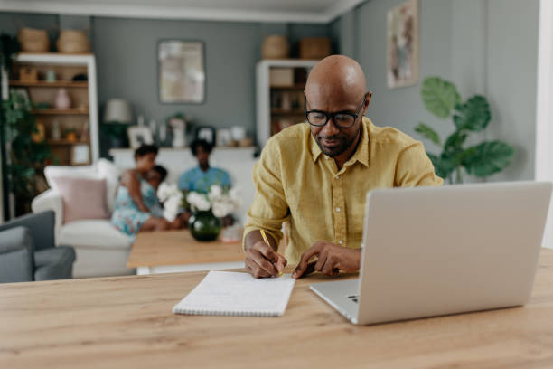 istock Man notes work on desk, family blurred in background. 2163634993