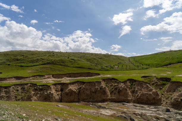 A hillside with a large crack in the ground. The sky is blue and there are clouds in the background