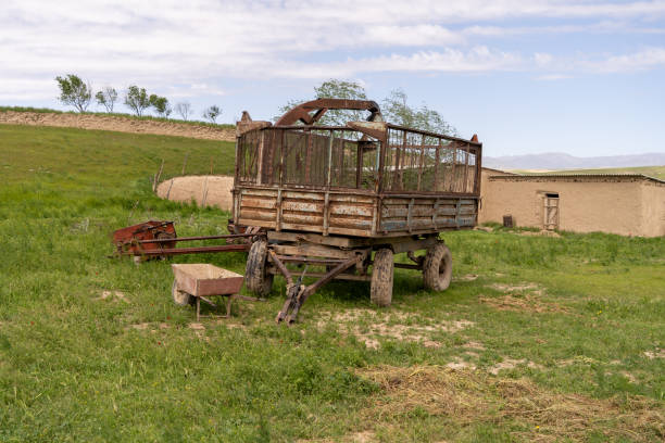 An old rusty farm truck is parked in a field. The truck is surrounded by a fence and is next to a barn. The scene is quiet and peaceful, with the only sounds being the rustling of the grass