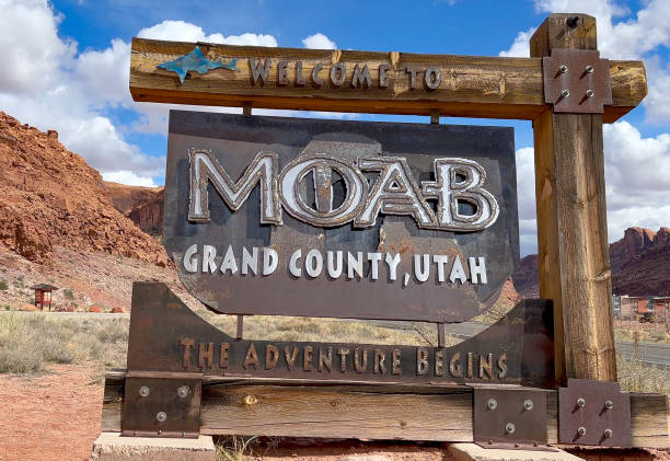 Welcome to Moab, Utah Adventure Sign in Front of Red Rock Mountains A welcome sign to Moab, Utah with red rock cliffs in the background. The Adventure Begins is written on the sign, inviting visitors to explore the area and all that it has to offer - USA canyonlands national park stock pictures, royalty-free photos & images