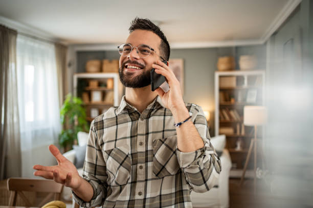 A handsome man with a beard is having a pleasant conversation on the phone at home