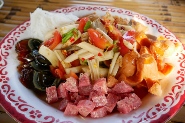 Mixed Thai Somtam It consists of Thai papaya noodles, tomatoes, chilies, and yardlong beans mixed with other ingredients such as century eggs, sausage, fermented pork, and khanom jeen. Everything is topped with papaya salad juice that tastes spicy, sour, sweet, and salty. somtam tailandés mixto consiste en fideos tailandeses de papaya, tomates, chiles y frijoles de yarda mezclados con otros ingredientes como huevos centenarios, salchichas, cerdo fermentado y khanom jeen. todo está cubierto con jugo de ensalada de papaya q
