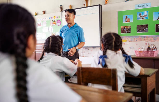 Rear view of a school classroom with students sitting on their seats and paying attention to the teacher teaching lesson