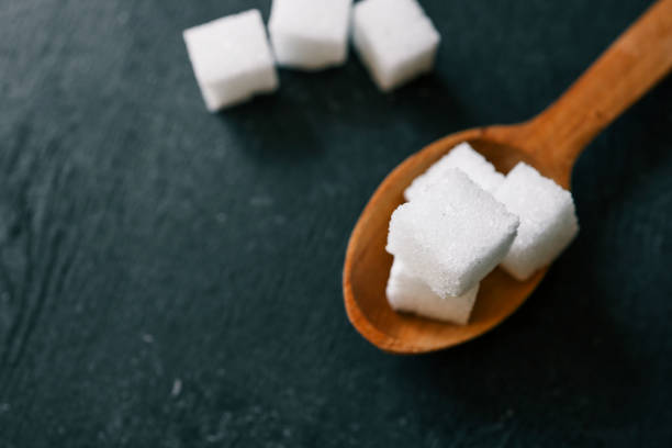 White crystalline sugar cubes on a wooden spoon.