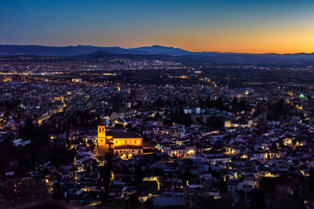 Elevated vantage point depicting the cityscape of the seaside city of Alicante in southern Spain at sunset. The city is bathed in warm light from the dazzling sunset.