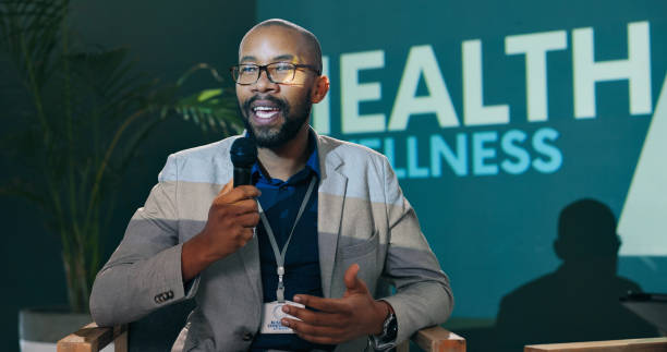 istock Speech, seminar and black man on microphone at stage with host or speaker at health event. Workshop, talk and conference presentation on wellness, pharma and medical innovation of drugs at convention 2163665320