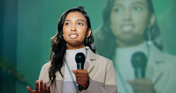 Conference, presentation or seminar and public speaking woman with microphone on stage for development speech. Business, podium and tradeshow with Indian motivational speaker in corporate auditorium