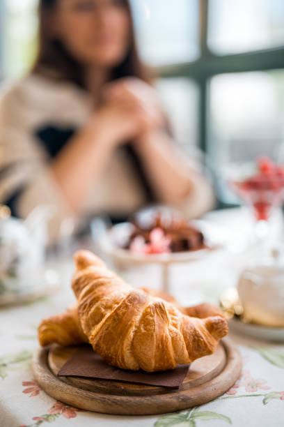 A woman enjoys a serene morning in a boutique hotel's restaurant, featuring a fresh croissant on a wooden plate, with stylish attire hinting at an upscale dining experience.