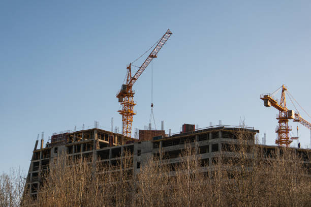 Construction site with cranes and scaffolding against a clear sky, indicating ongoing urban development