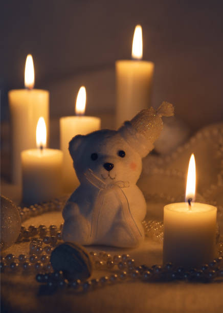 White bear with a hat, surrounded by lit candles, beads, and baubles in a cozy, festive setting