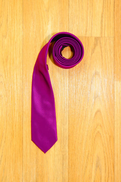 istock Plain fabric purple color necktie rolled on wooden background close-up view single object 2163676284