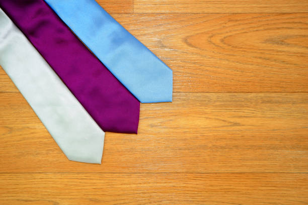 Plain fabric colour neckties layered together side by side with wooden background