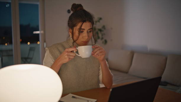 istock Evening freelancer drinking coffee looking laptop at home workplace closeup 2163680692
