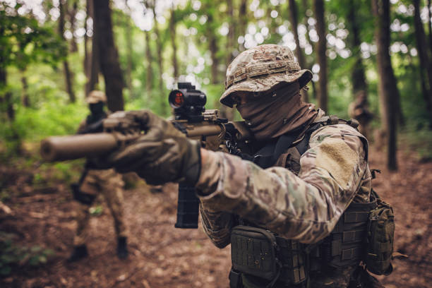 istock Camouflaged soldier in dense forest aiming rifle. 2163682497