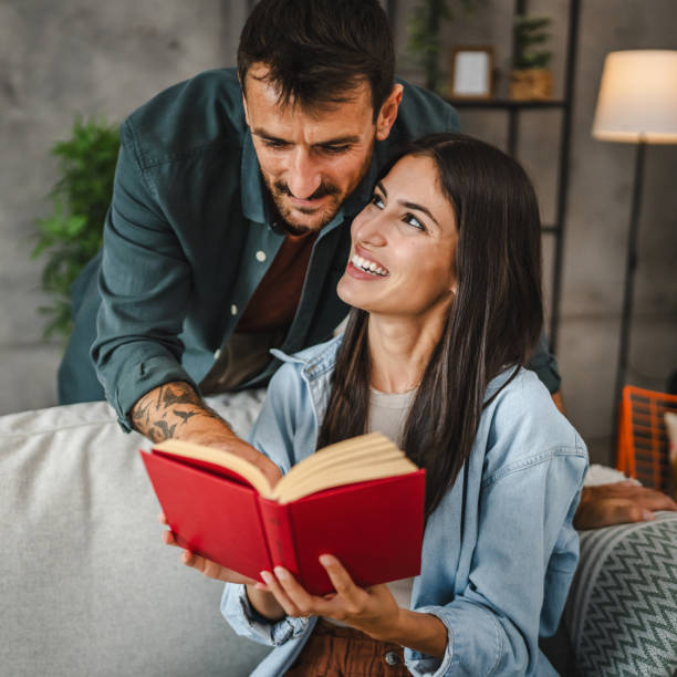 istock girlfriend sit on sofa and read a book while boyfriend hug her 2163682880