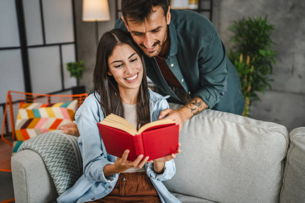 istock girlfriend sit on sofa and read a book while boyfriend hug her 2163683382